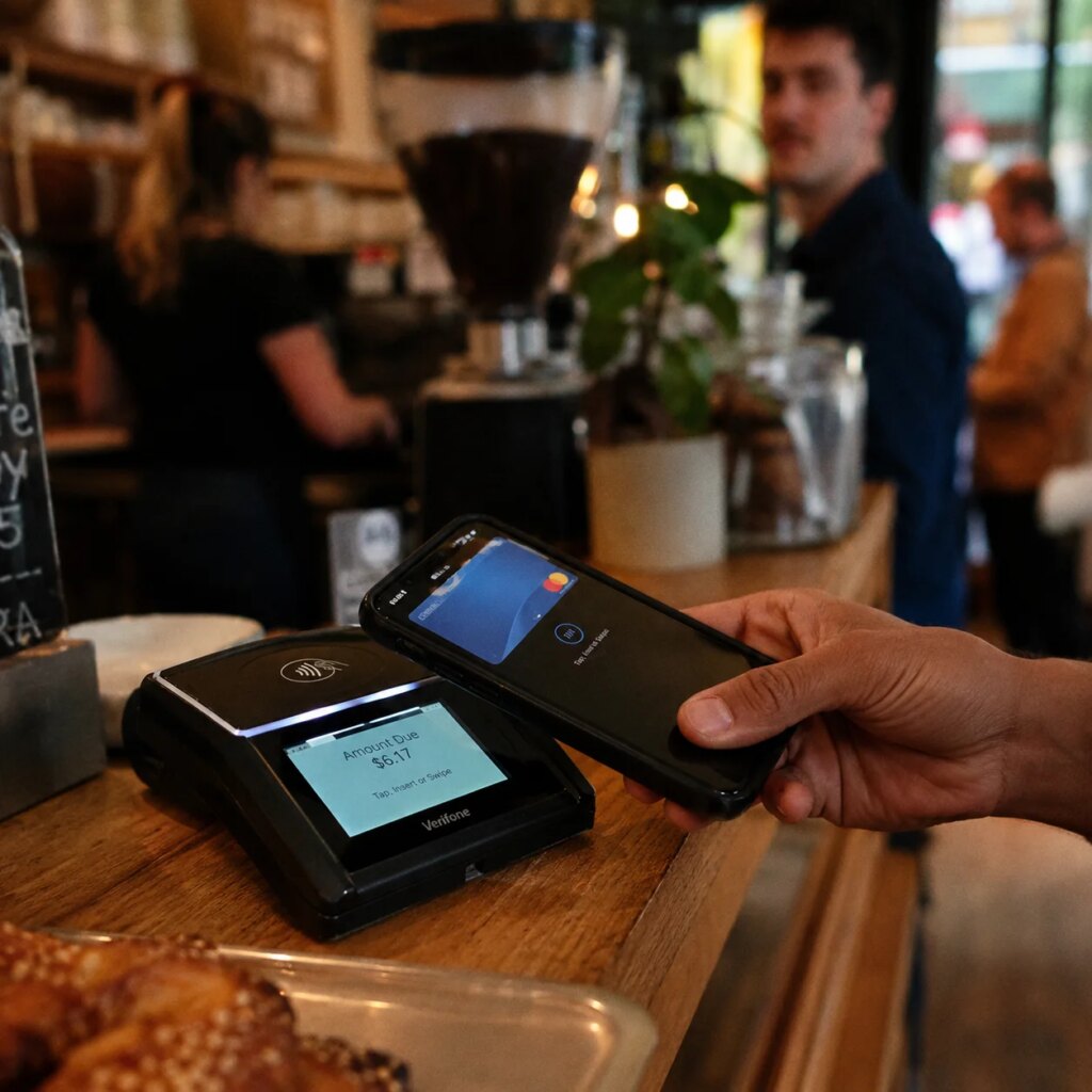 Person tapping smartphone on contactless payment terminal at a café counter in New York City